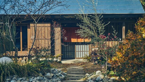 A rustic wooden building with a metal roof, surrounded by a garden with a stone pathway leading to the entrance. - Kominka Yado Loof Sawanoie (Fuefuki)