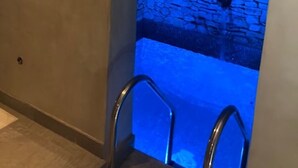 Paredede pedra com luz azul, um pequeno recanto e uma cadeira de metal.