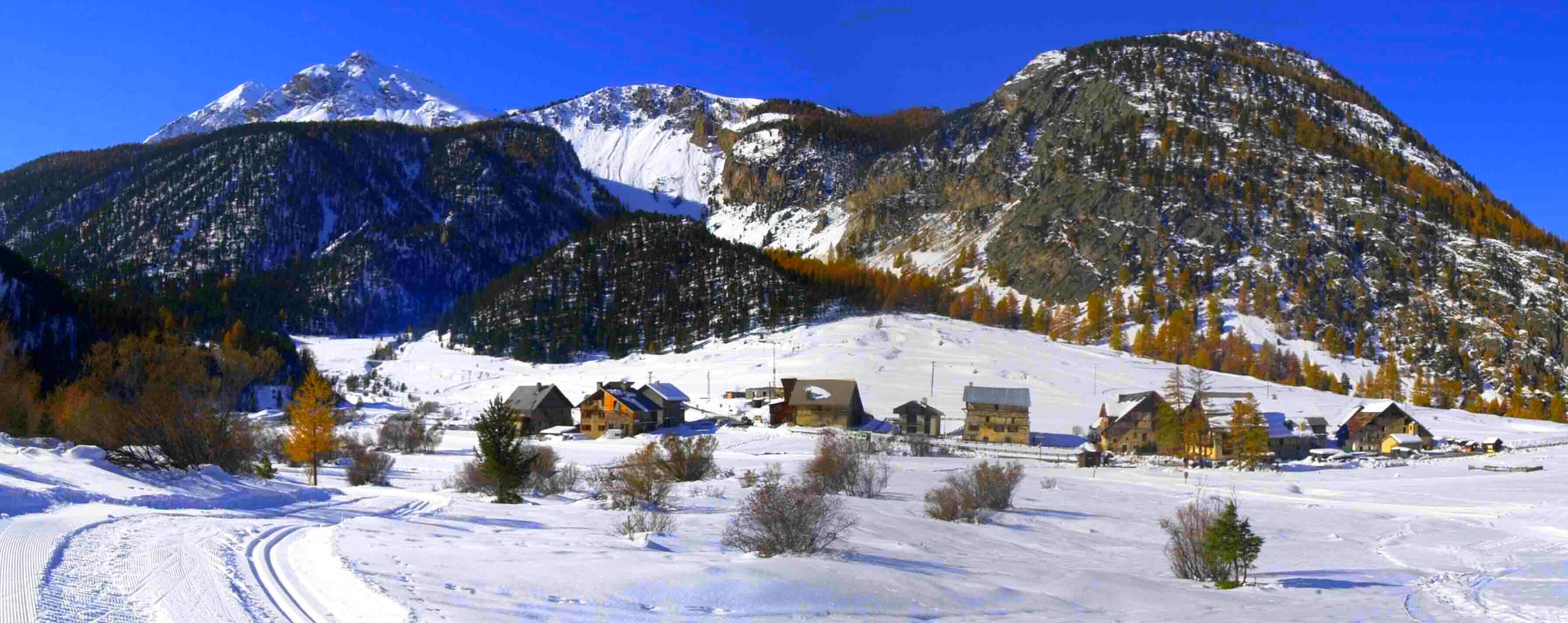 A snow-covered mountain village with traditional houses, a clear sky, and a ski trail.