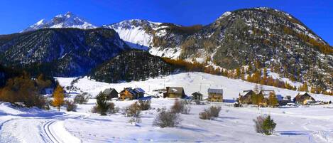 A snow-covered mountain village with traditional houses, a clear sky, and a ski trail.