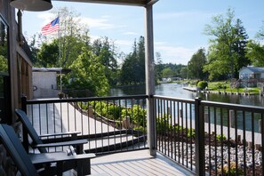 A wooden deck with a railing, overlooking a river, with an American flag visible. - Brand New 3BR River Condo w/ Large Terrace (Indian River)