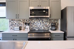 A kitchen with grey cabinets, a microwave, a coffee maker, and a toaster. - Brand New 3BR River Condo w/ Large Terrace (Indian River)