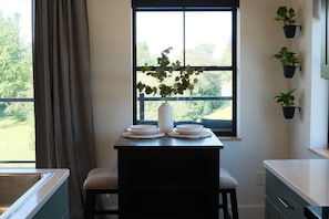 Une cuisine avec une fenêtre, un vase avec des plantes et une vue sur la verdure à l’extérieur.