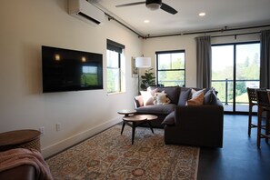 A living room with a flat-screen TV, a sofa, a coffee table, and a patterned rug. - Brand New 2BR River Condo w/ Large Terrace (Indian River)