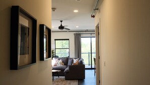 A hallway leading to a living room with a sofa, a ceiling fan, and a large window.