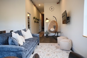 Una sala de estar con sofá azul, una silla colgante, un tapete estampado y un reloj de pared.