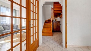 Ein Flur mit einer Holztreppe, einer Glastür und Blick auf ein Wohnzimmer mit Sofa und Teppich.