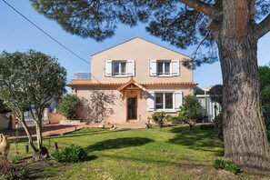 Una casa de dos pisos con un porche delantero, un pequeño jardín y un árbol grande.