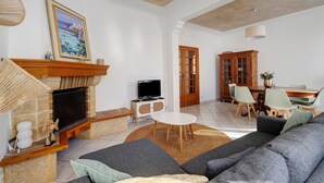 Ein Wohnzimmer mit Kamin, Sofa, Fernseher, Esstisch und Stühlen.