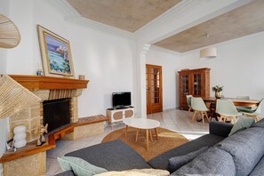 A living room with a fireplace, sofa, TV, dining table, and chairs. - Charming Pornic House with Garden (Pornic)