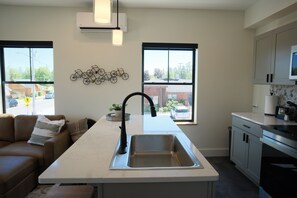 A modern kitchen with a central island, a built-in sink, and a dining area with a sofa. - New 2BR Condo in Heart of Indian River! (Indian River)