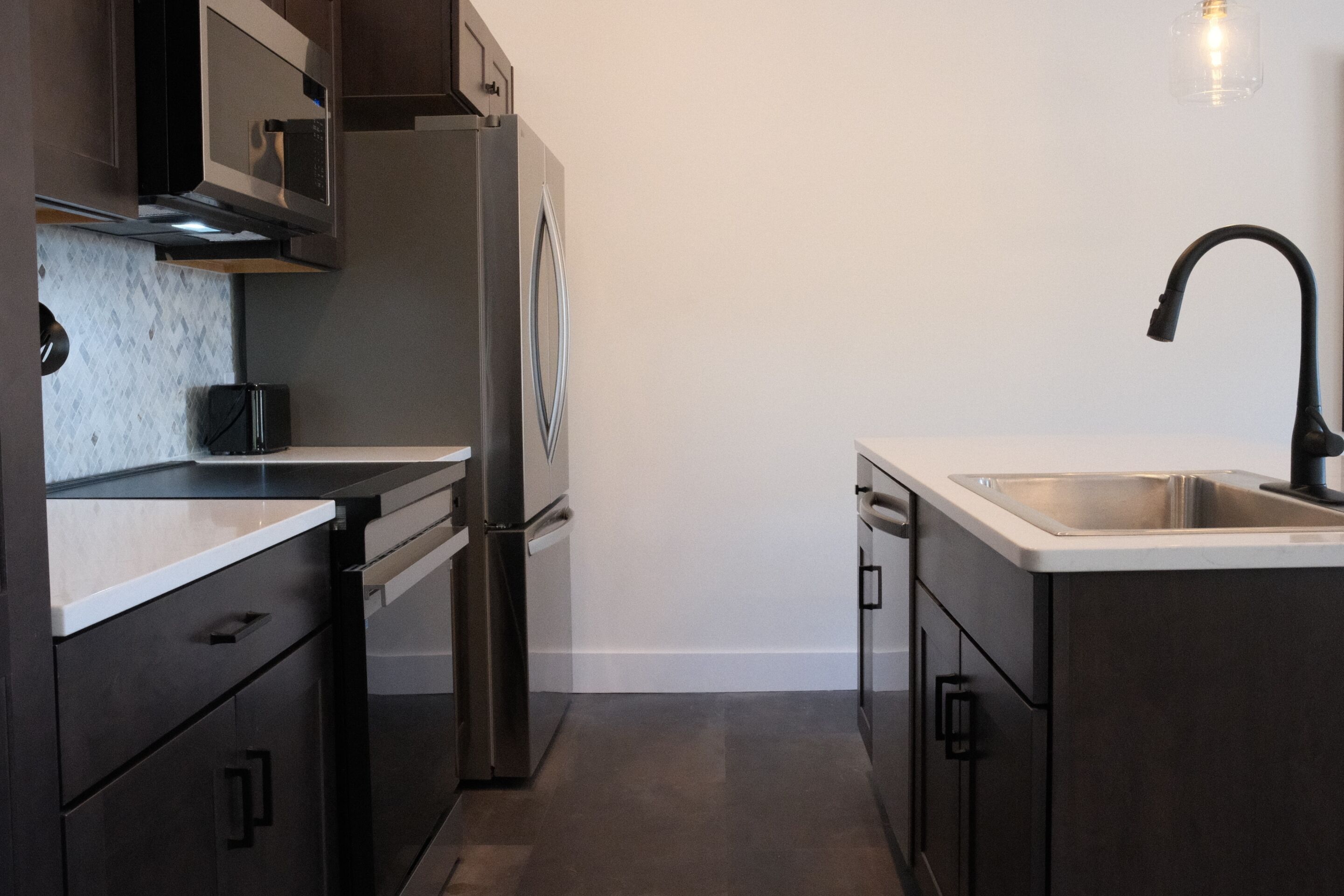A modern kitchen with dark cabinetry, stainless steel appliances, and a white countertop.