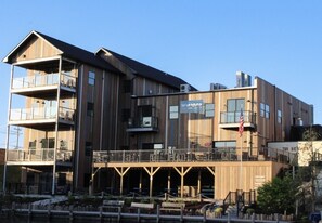 A multi-story building with balconies, a covered outdoor seating area, and a sign indicating a restaurant. - New 2BR River Condo w/ Balcony (Indian River)