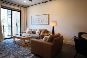A living room with a sofa, a coffee table, a lamp, and a painting on the wall. - New 2BR River Condo w/ Balcony (Indian River)