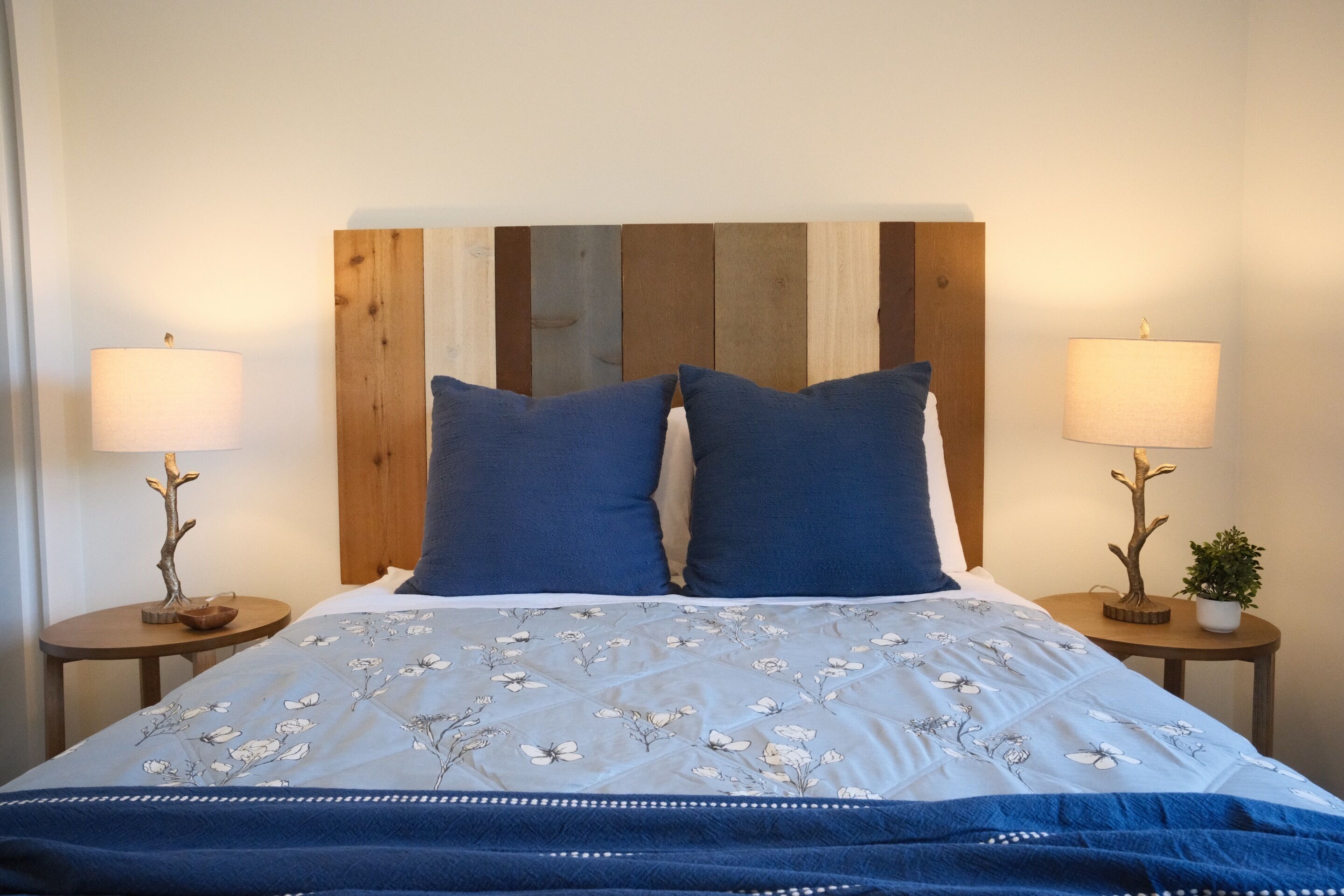 Ein Bett mit einem blumigem Überwurf, zwei passende Kissen und einem Holz-Kopfstück.