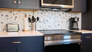 A modern kitchen with dark cabinets, a microwave, a coffee maker, and a countertop with a patterned backsplash.