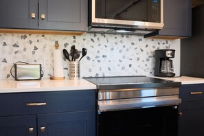 Une cuisine moderne avec des meubles de couleur sombre, un four à micro-ondes, une machine à café et un plan de travail agrémenté d’un pare-feu décoratif.
