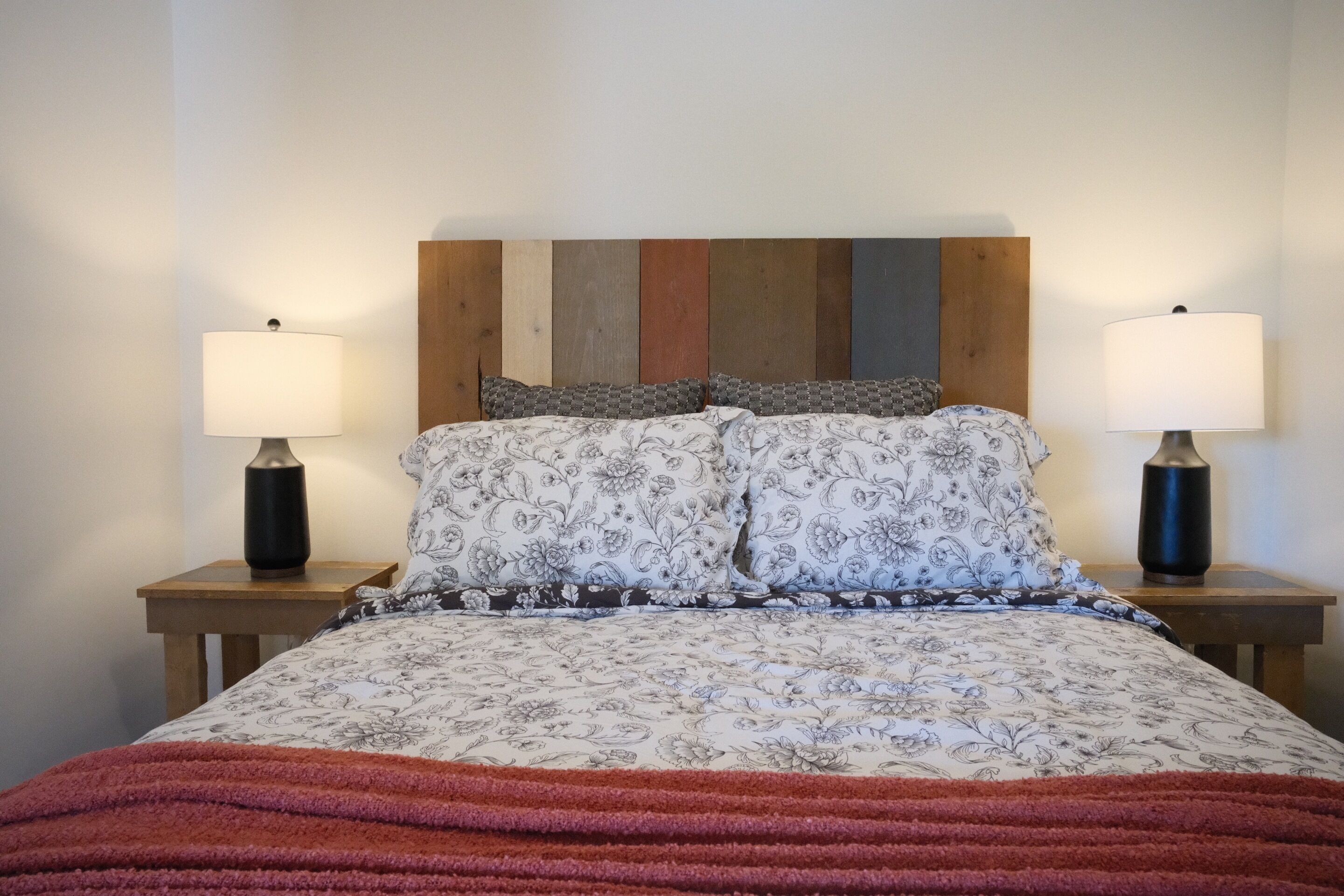 A bed with floral bedding, two bedside lamps, and a wooden headboard.