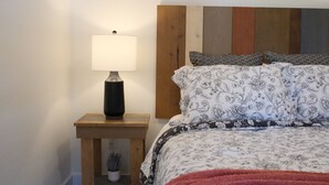 A bedroom with a wooden headboard, a bedside table with a lamp, and a floral-patterned bedspread.