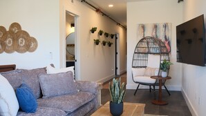 Een woonkamer met een bank, een salontafel, een hangstoel en een aan de muur bevestigde televisie.