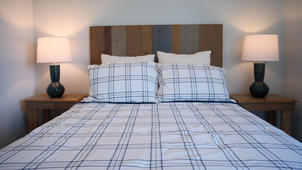 Een bed met een geruite plaid, twee nachtkastjes met lampen, en een houten hoofdbord.