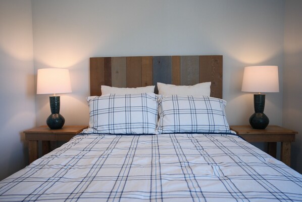 A bed with a plaid bedspread, two bedside tables with lamps, and a wooden headboard.