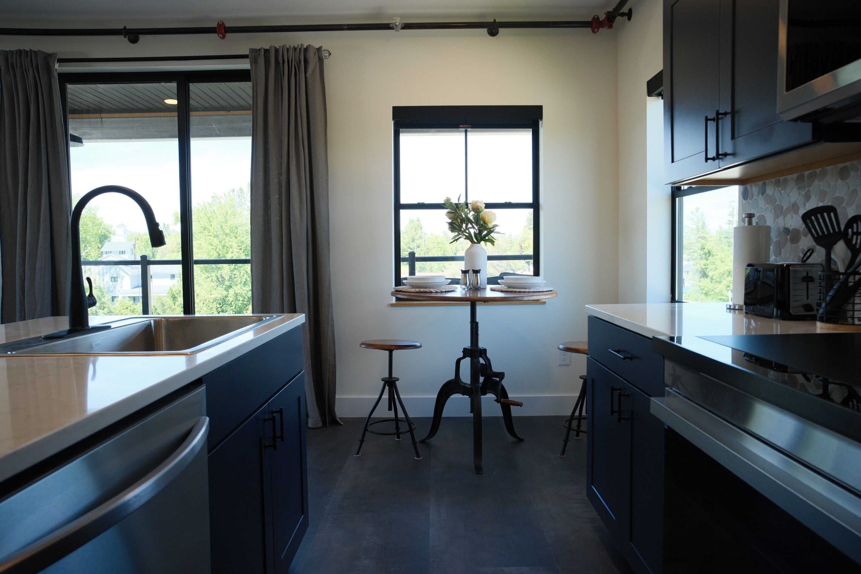 A modern kitchen with a large window, a sink, and a dining area with stools.