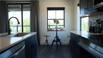 A modern kitchen with a large window, a sink, and a dining area with stools.