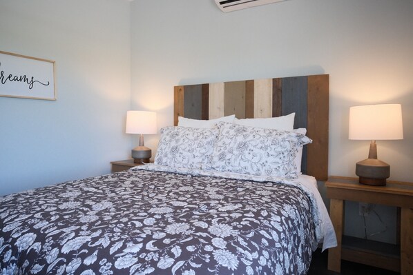A neatly made bed with a floral bedspread, two bedside lamps, and a wall-mounted sign.