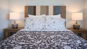 Una cama con colcha de estampado floral, cabecera de madera y dos lámparas de noche.