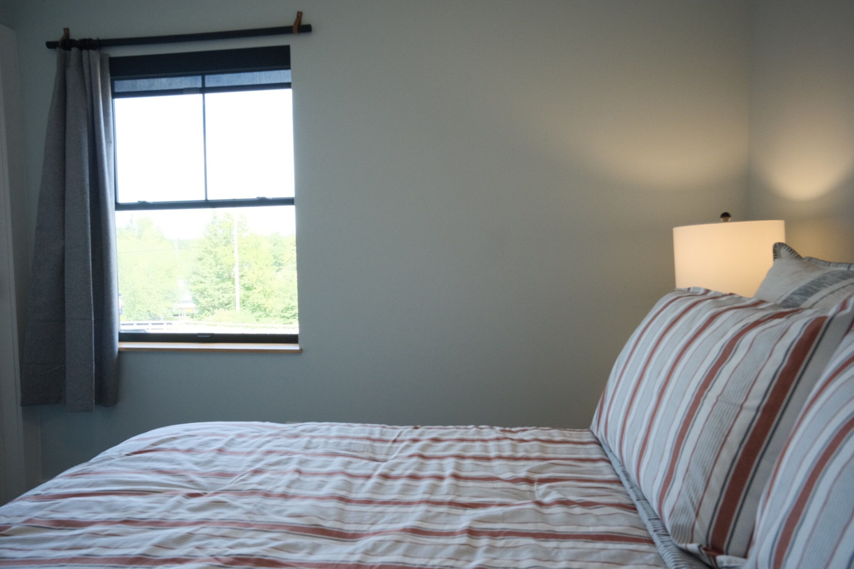 A bedroom with a bed, a window with curtains, and a bedside lamp.