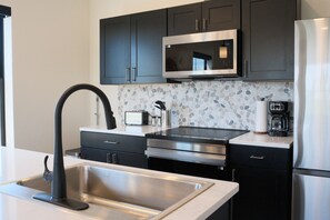 Une cuisine moderne avec des meubles de couleur sombre, des appareils en acier inoxydable, un pare-feu en granit et un robinet noir.