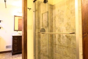 A bathroom with a glass shower enclosure, a wooden vanity with drawers, and a tiled floor. - Astor Street Retreat 3BR Condo (Mackinac Island)