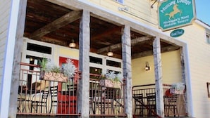 Ein Gebäude mit der Aufschrift "The Mustang Lounge", das auf einem Steinfundament ruht, Holzbalkone aufweist und eine Außenbestuhlung mit Metallgeländern bietet.