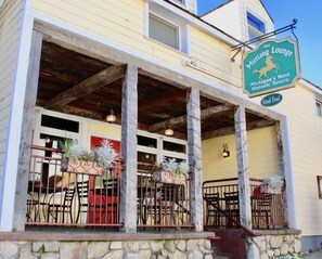 A building with a sign reading "The Mustang Lounge," featuring a stone foundation, wooden beams, and outdoor seating with metal railings. - Astor Street Retreat 3BR Condo (Mackinac Island)