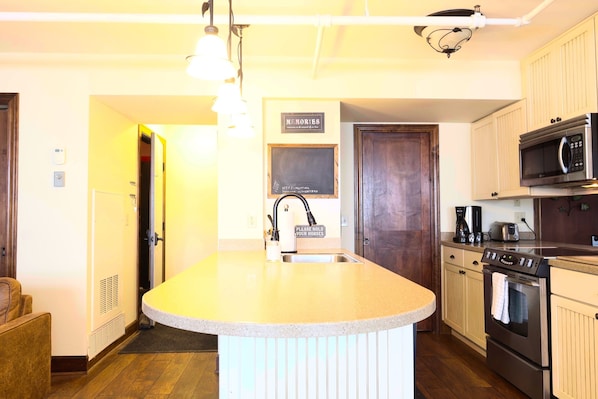 A kitchen with a central island, stainless steel appliances, and a chalkboard sign.