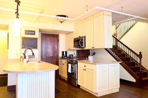 Une cuisine dotée d’un îlot central, d’appareils électroménagers en acier inoxydable et d’un escalier en bois.