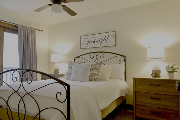 A bedroom with a bed, bedside lamps, a nightstand, a wooden dresser, and a ceiling fan. - Astor Street Retreat 3BR Condo (Mackinac Island)