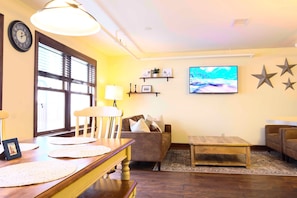 A living room with a wooden dining table, a sofa, a TV, and decorative shelves.