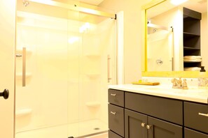 Une salle de bain moderne avec une douche à l’italienne en verre, un lavabo blanc avec un miroir au-dessus et des meubles aux tons foncés.