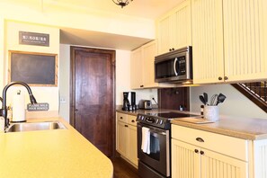 A kitchen with a sink, stove, microwave, and cabinets. There is a chalkboard on the wall and a sign that says "Please hold your horses".