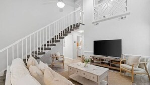 Ein geräumiges Wohnzimmer mit Treppe, Flachbildfernseher und einer gemütlichen Sitzecke.