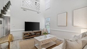 Ein modernes Wohnzimmer mit einem Flachbildfernseher, einem Holztisch und einem weißen Sofa.