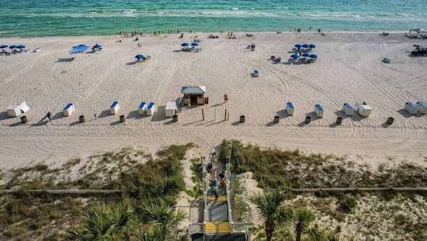 Ein Strand mit Reihen von Liegestühlen und Sonnenschirmen, einem Rettungsturm und einem sandigen Weg zum Wasser.
