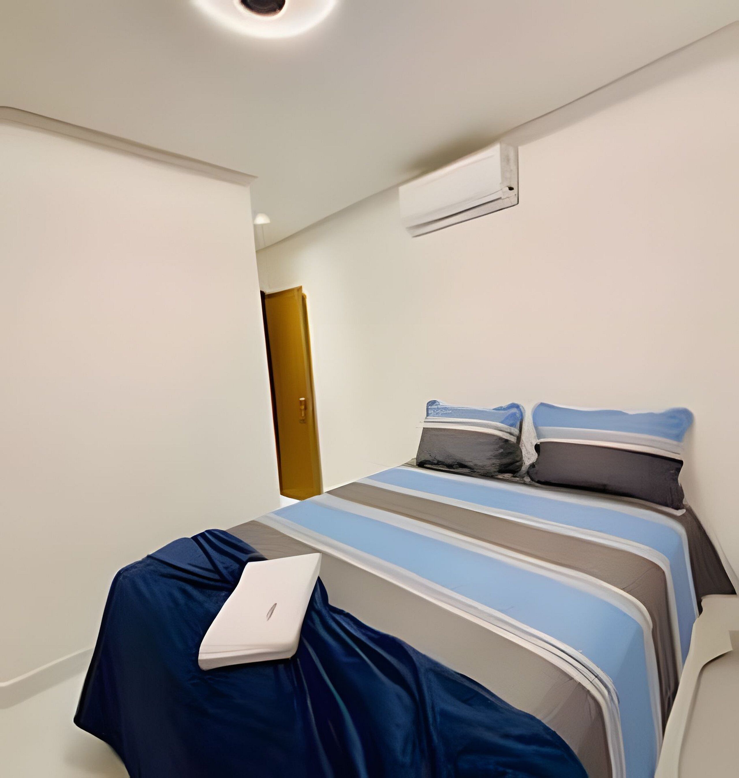 A modern bedroom with a bed, pillows, a laptop, and an air conditioning unit.