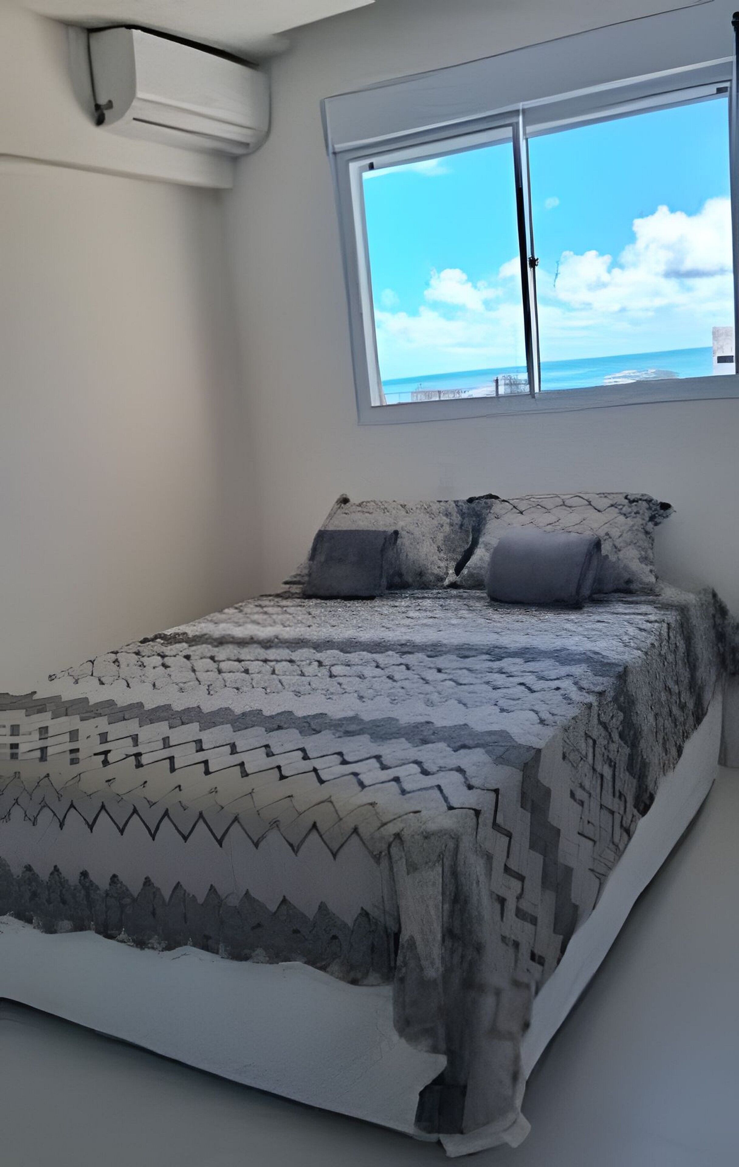 Un dormitorio con una cama, una ventana con vista al mar y una pared blanca.