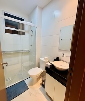 A modern bathroom with a toilet, sink, and glass shower enclosure.