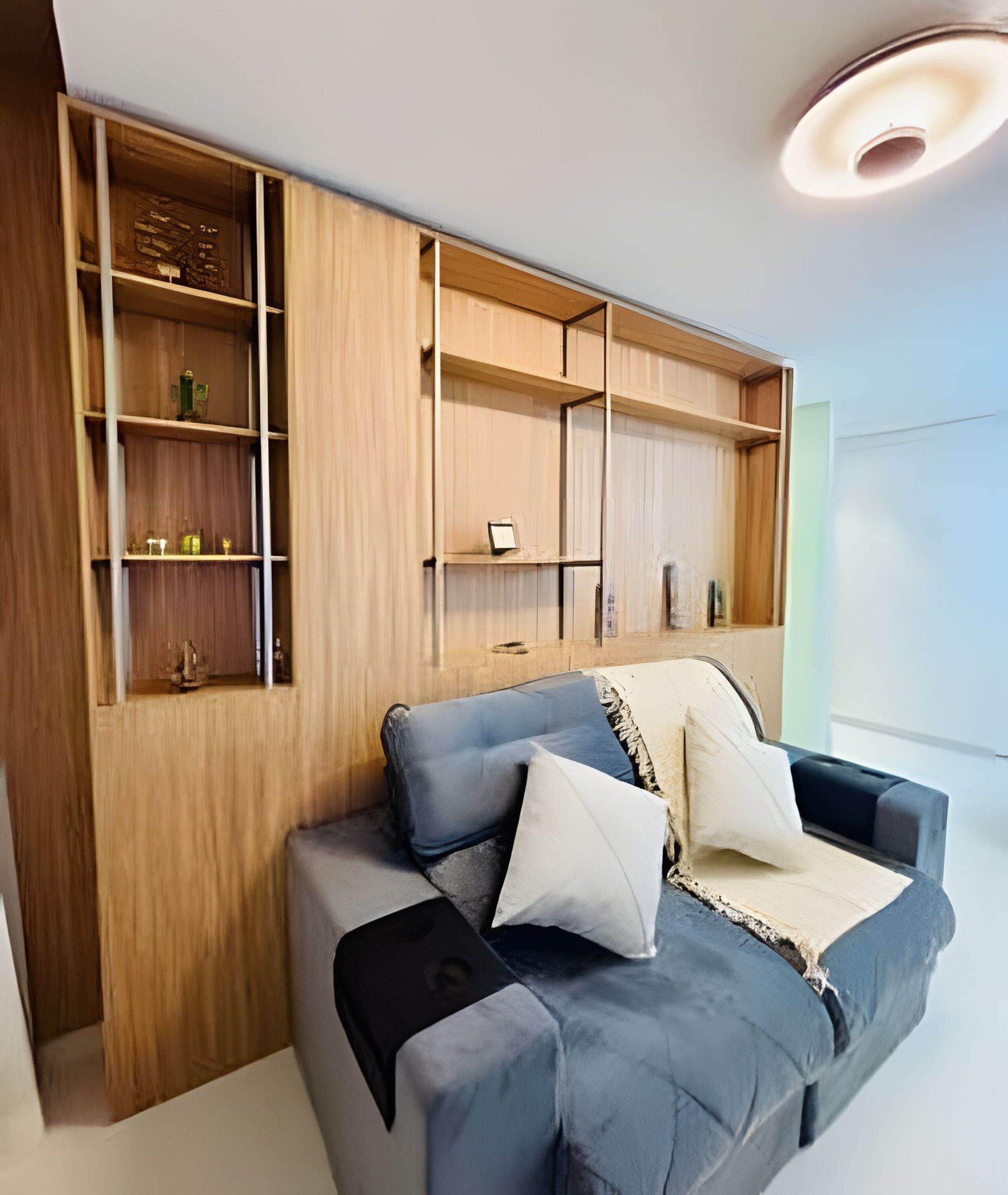 Una sala de estar moderna con una estantería empotrada de madera, un sofá gris con cojines y una lámpara de techo.