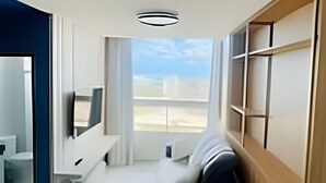 Una sala de estar moderna con un sofá, un televisor y vistas del cielo a través de un ventanal grande.