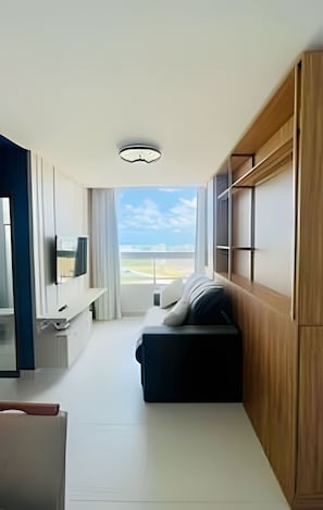 A modern room with a sofa, a flat-screen TV, and a large window offering a view of the sky and landscape. - 1501 Apto2 Qtos Vista Mar (Cabedelo)